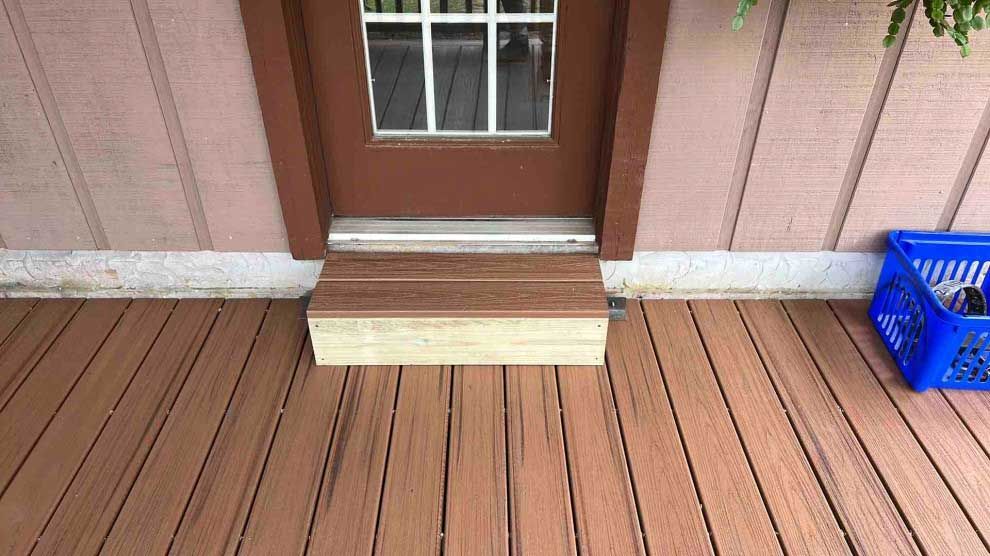 A wooden deck with steps leading to a door and a blue basket.