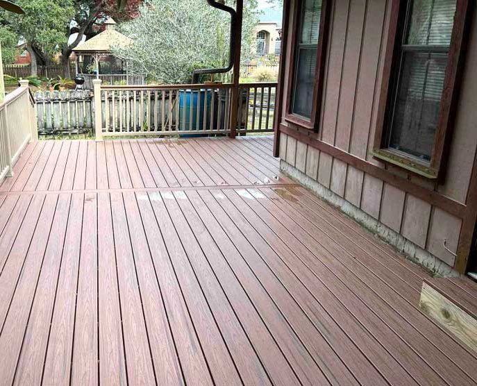 A large wooden deck with a railing in front of a house.
