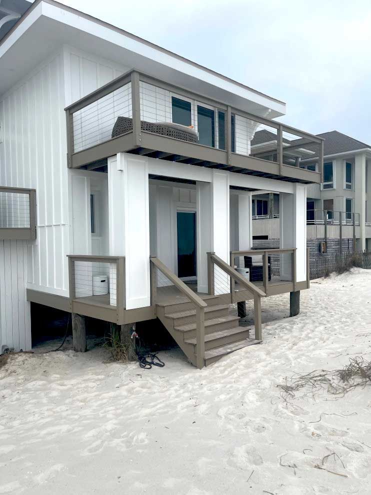 A white house with a deck and stairs on the beach.