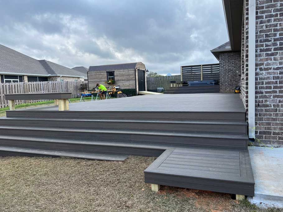 A large deck with stairs leading up to it is in front of a house.