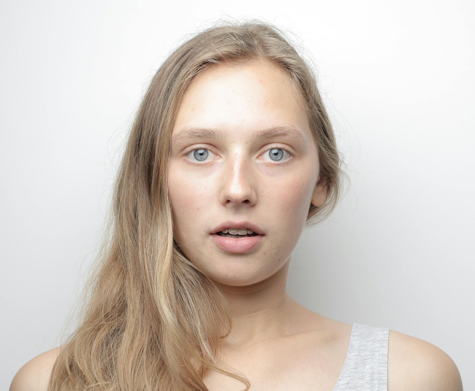 A woman with long blonde hair and blue eyes is making a surprised face.