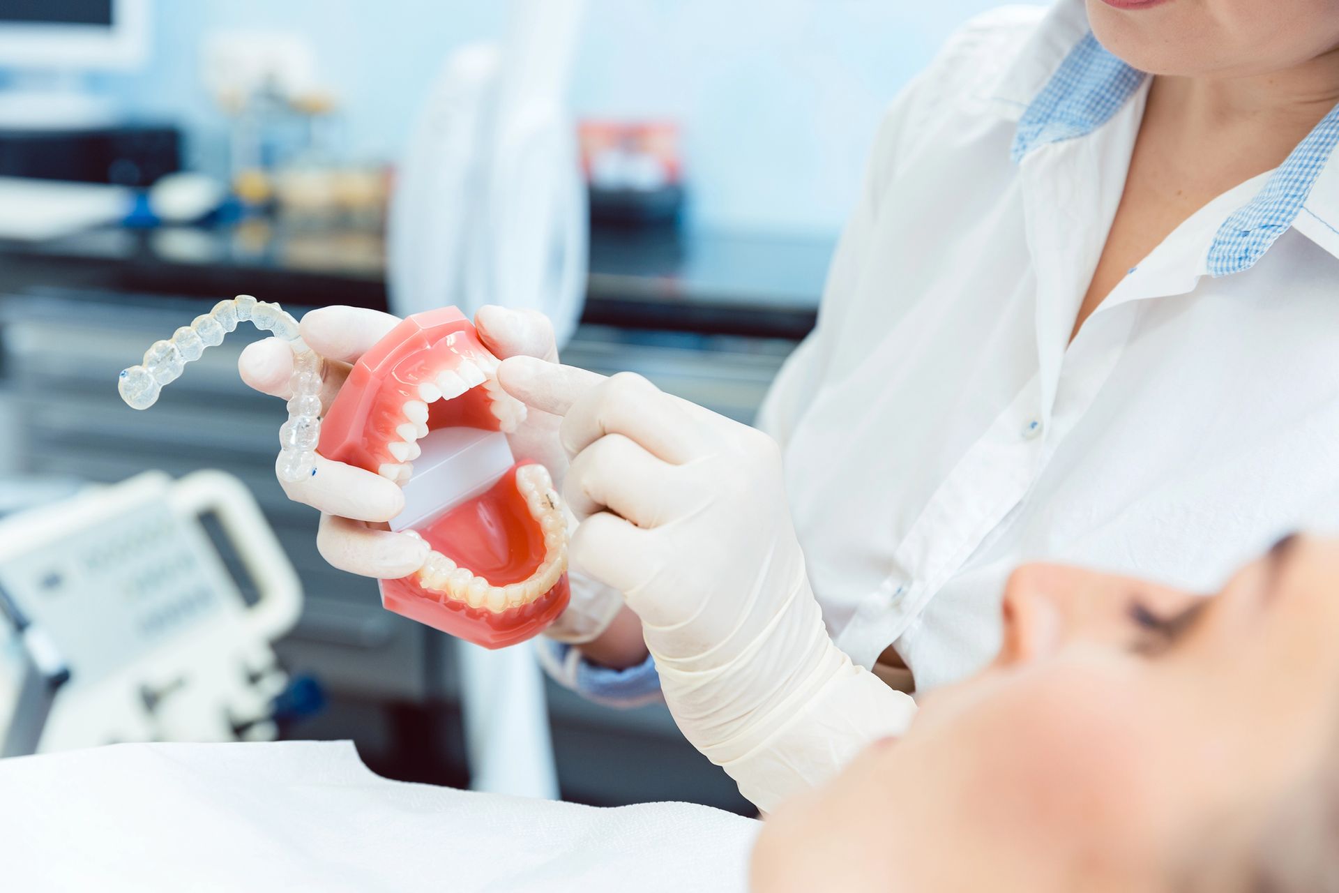 Un dentista sostiene un modelo dental con un paciente recostado en la silla cerca.