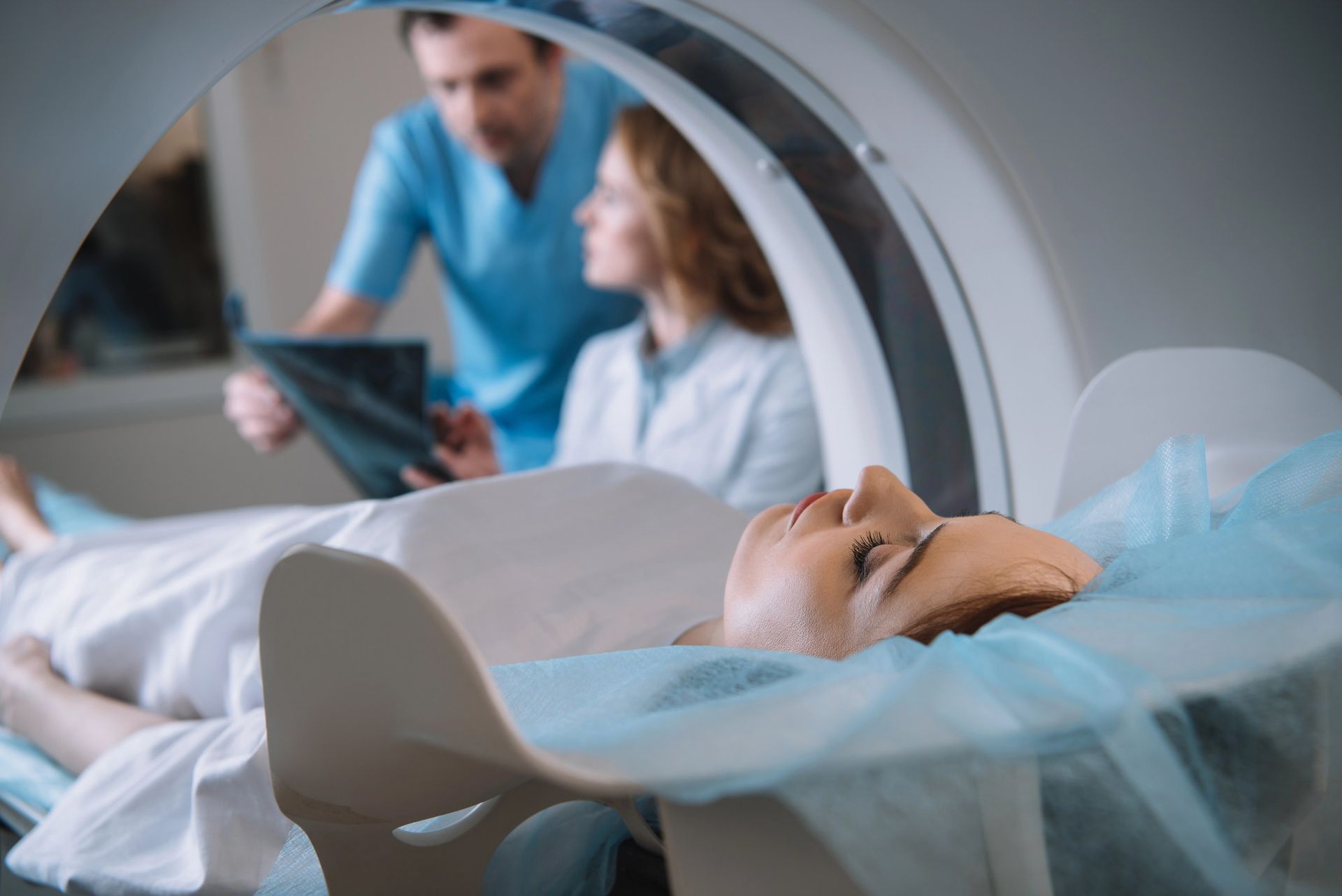 Persona sdraiata esame  tac scanner medico, due operatori sanitari osservano la scansione.