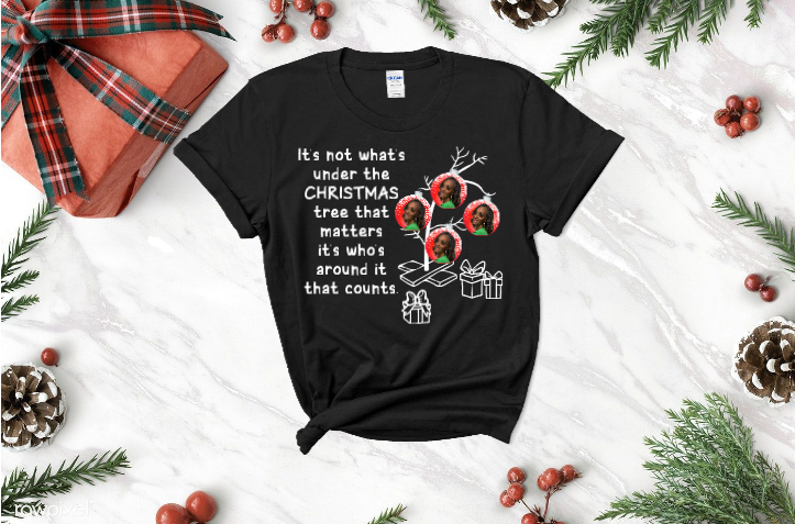 A black t-shirt with a christmas tree on it is sitting on a table surrounded by christmas decorations.