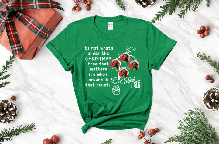 A black t-shirt with a christmas tree on it is sitting on a table surrounded by christmas decorations.