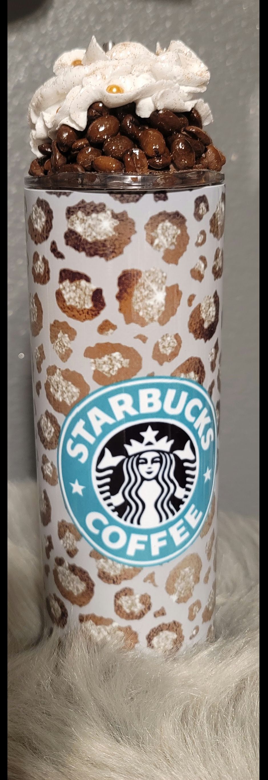 A starbucks coffee cup with a leopard print and whipped cream on top.