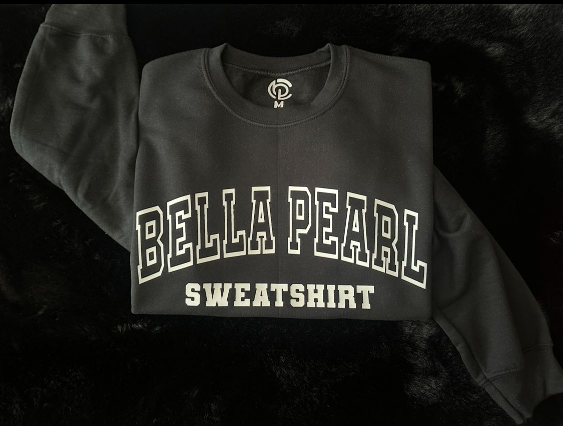 A black bella pearl sweatshirt is laying on a black surface