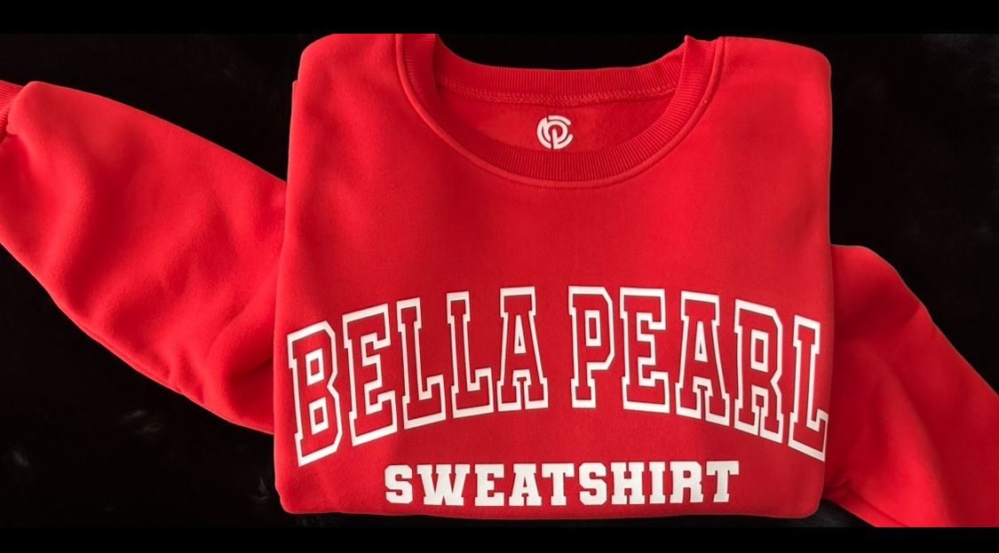 A red bella pearl sweatshirt is folded up on a black surface.