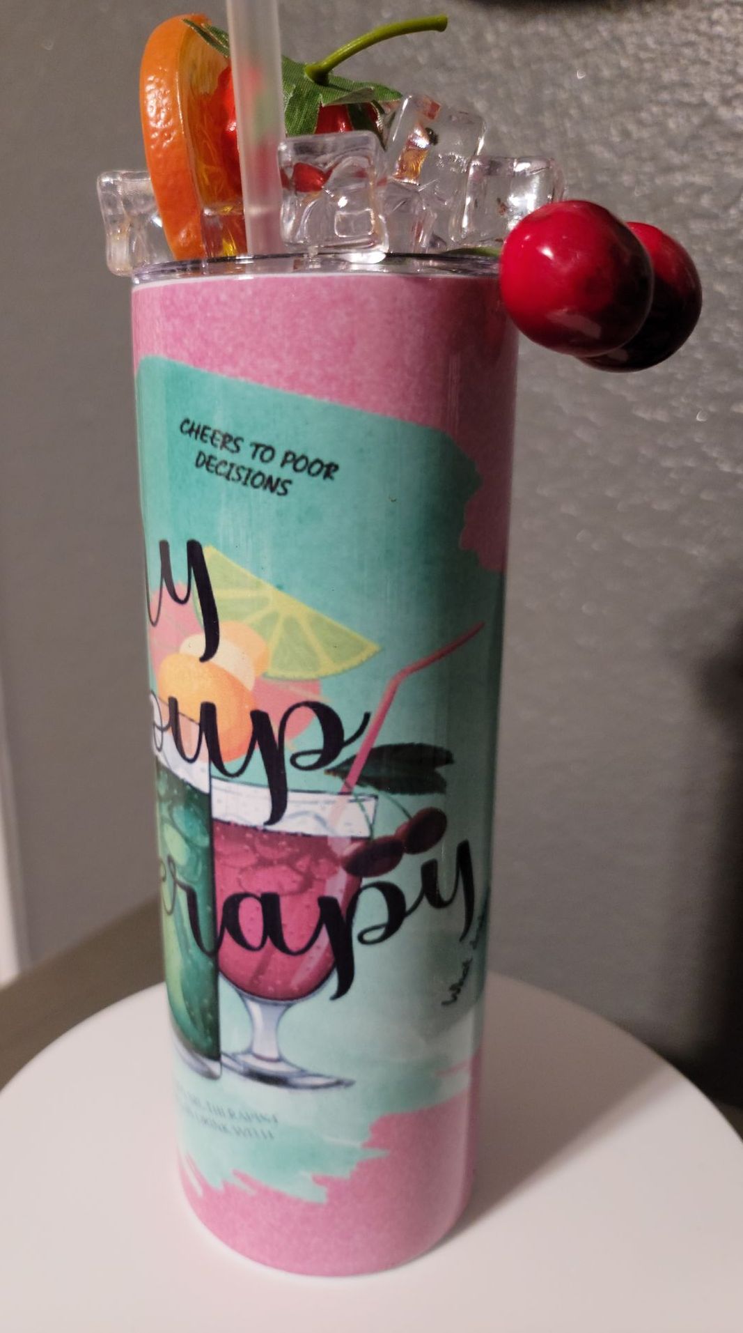 A pink tumbler with a straw and a cherry on it is sitting on a table.