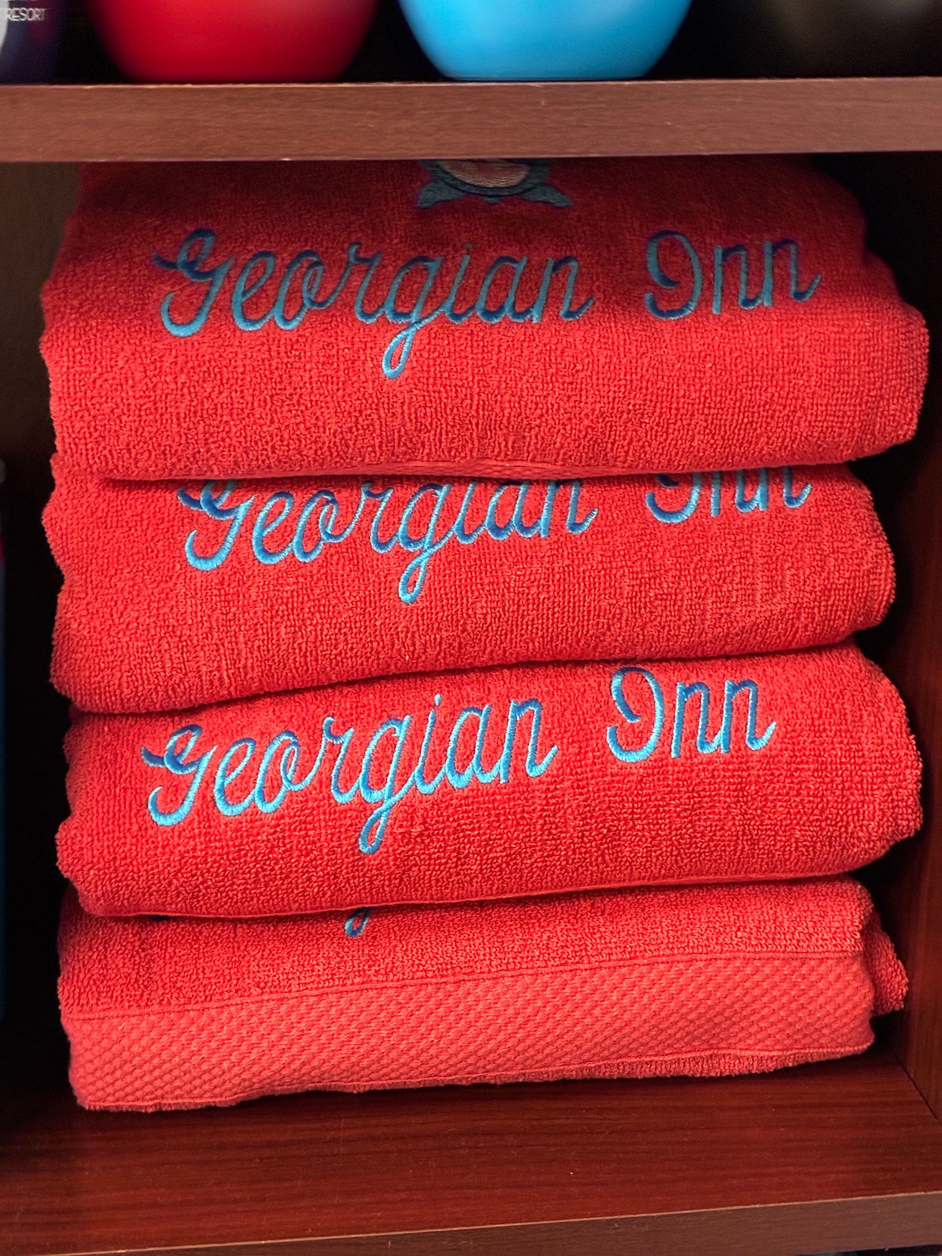 Red towels stacked on a shelf, embroidered with 