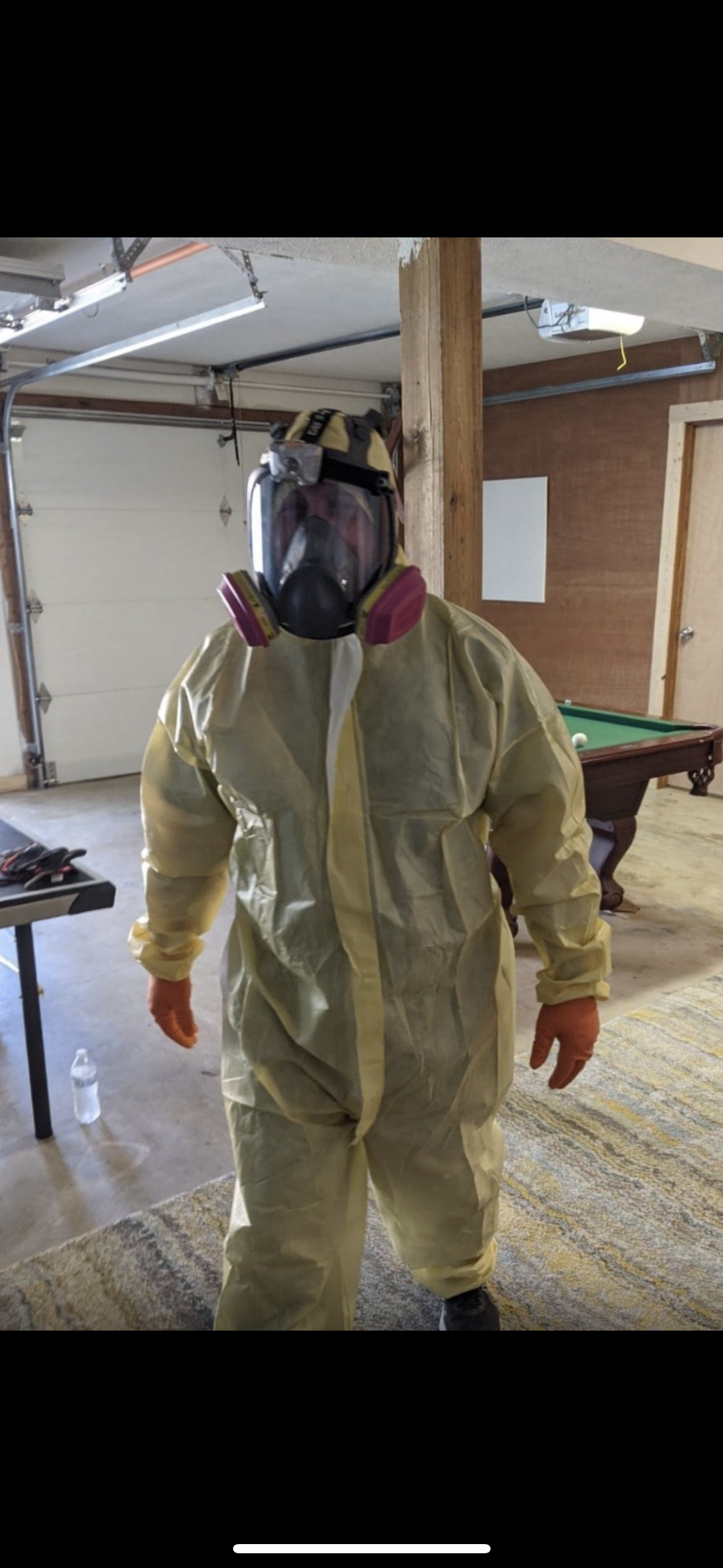 A person wearing blue gloves is pointing at mold on a wall.