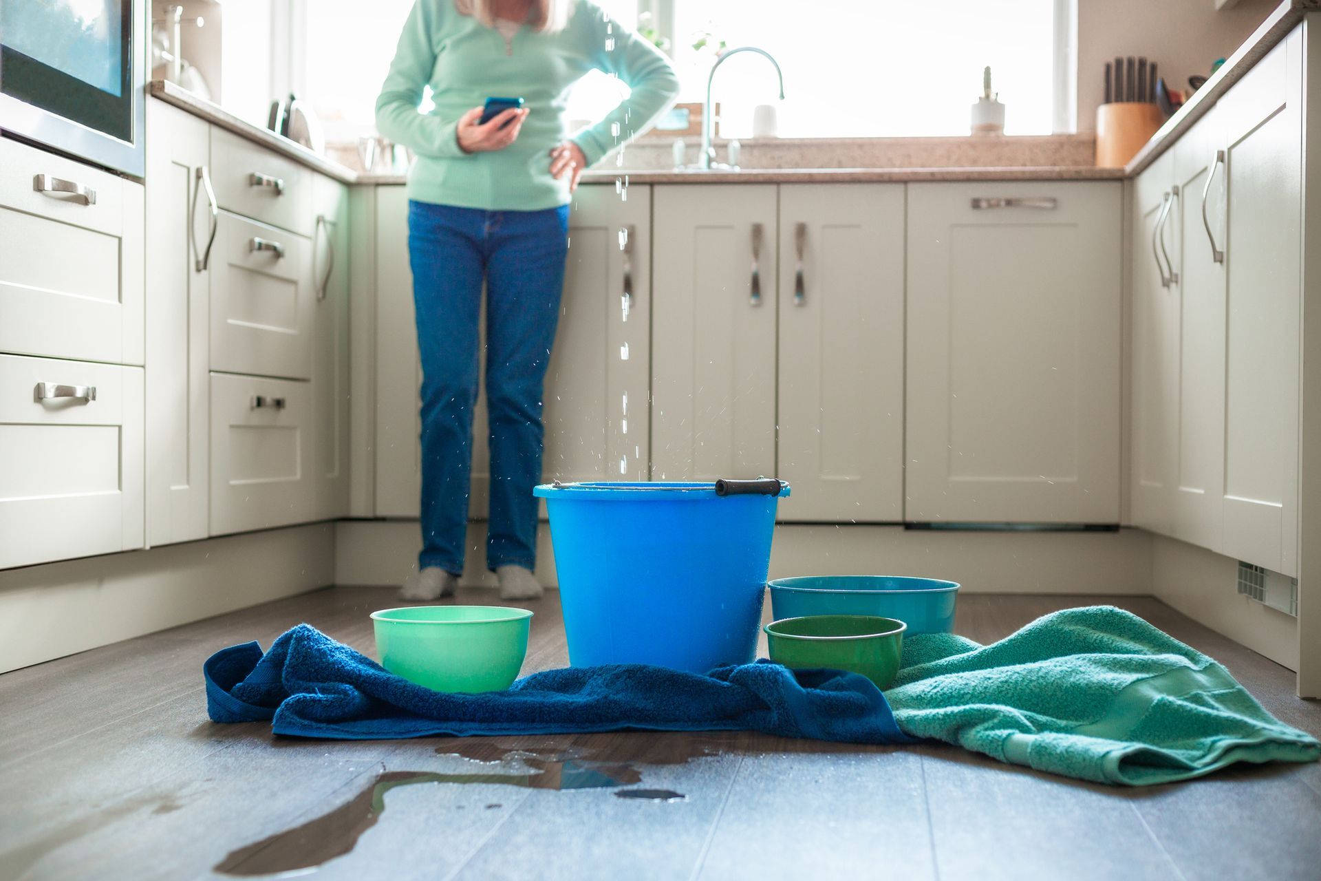 A woman is standing in a kitchen next to a bucket of water.