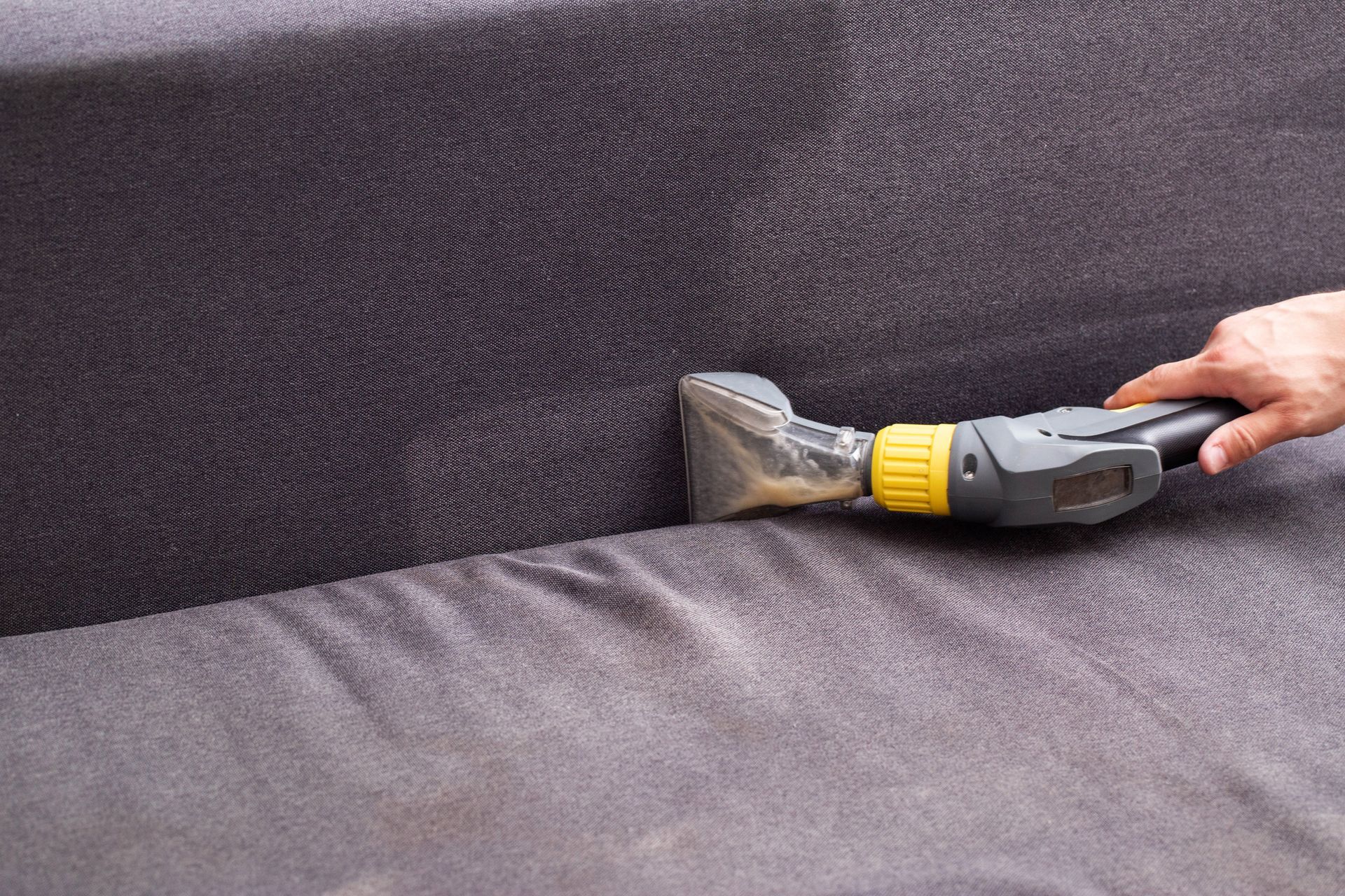 A person is cleaning a couch with a vacuum cleaner.