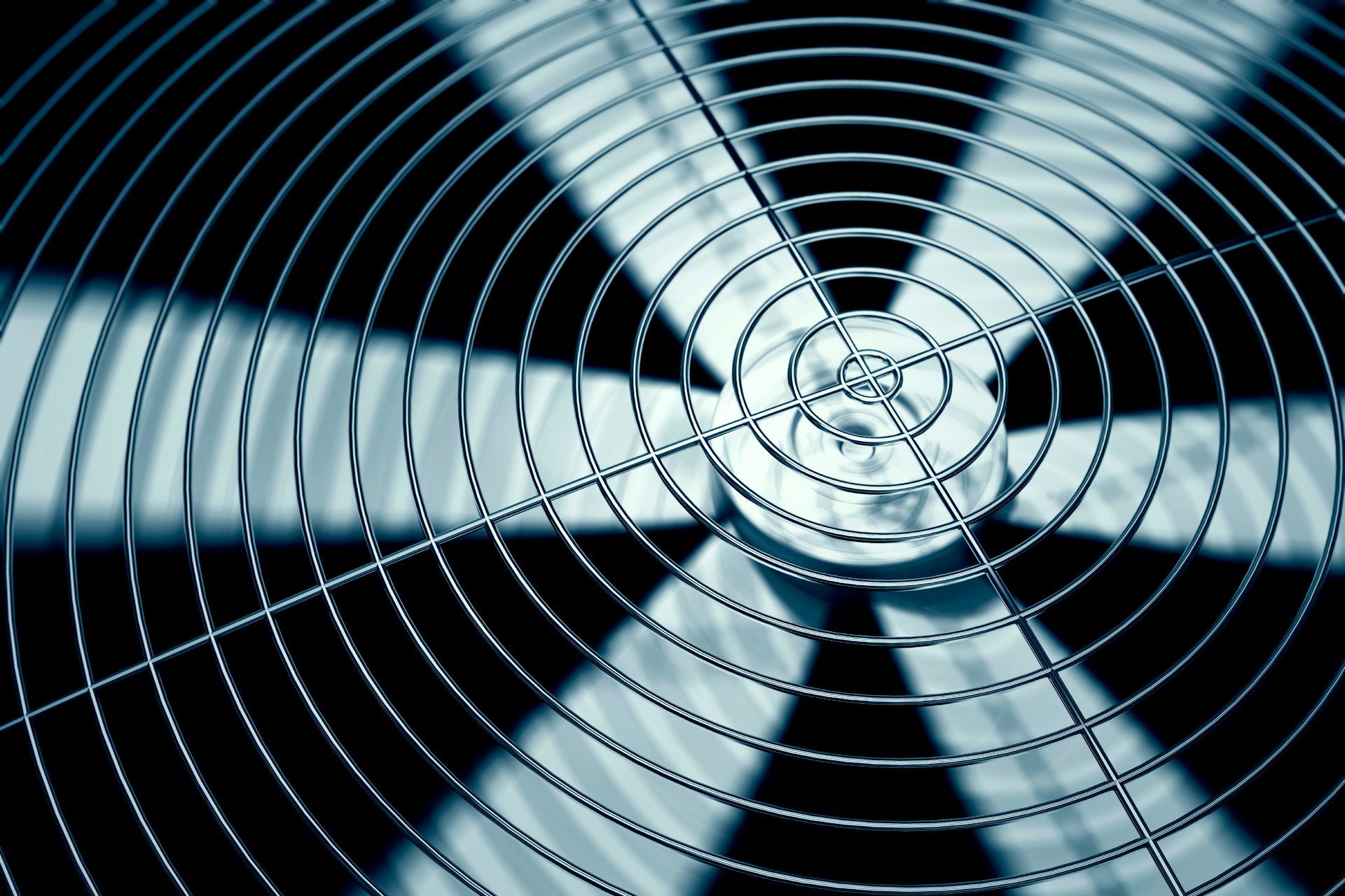 Close-up of a metal fan grille with spinning blades in blue-gray tones