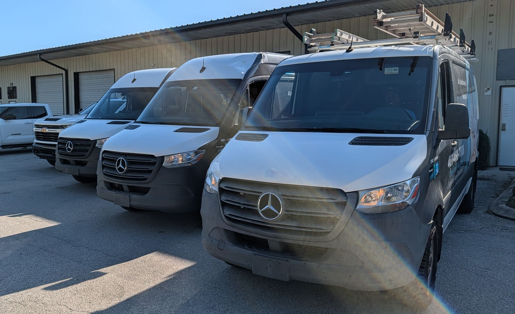 Three gray Mercedes vans parked in front of a warehouse in bright sunlight.