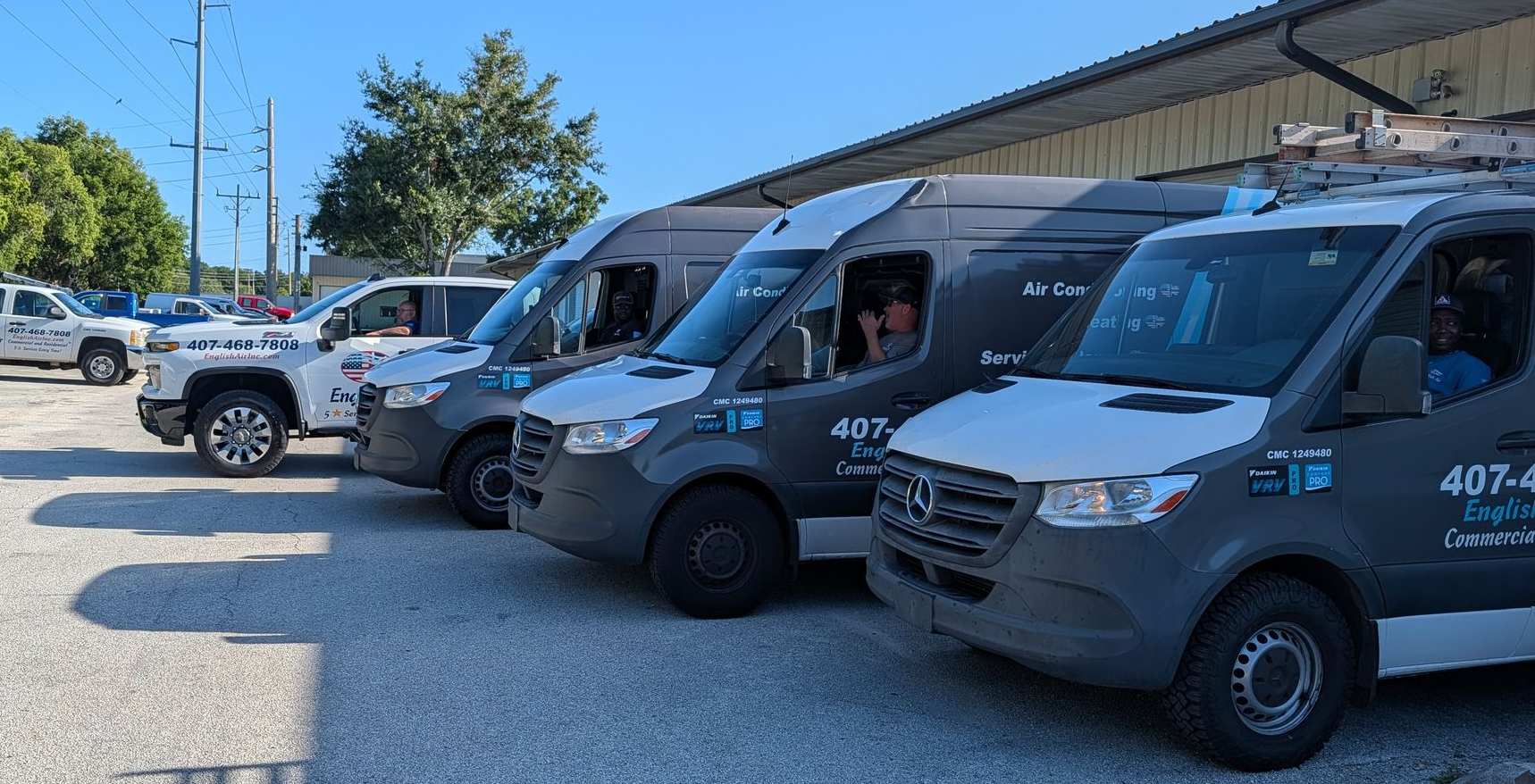 Row of gray delivery vans parked outside a warehouse on a sunny day