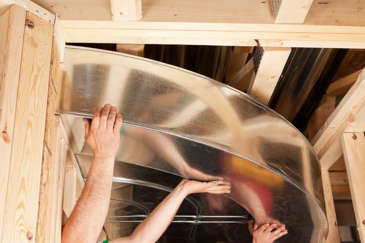 Person installing shiny insulation in a wooden attic ceiling frame