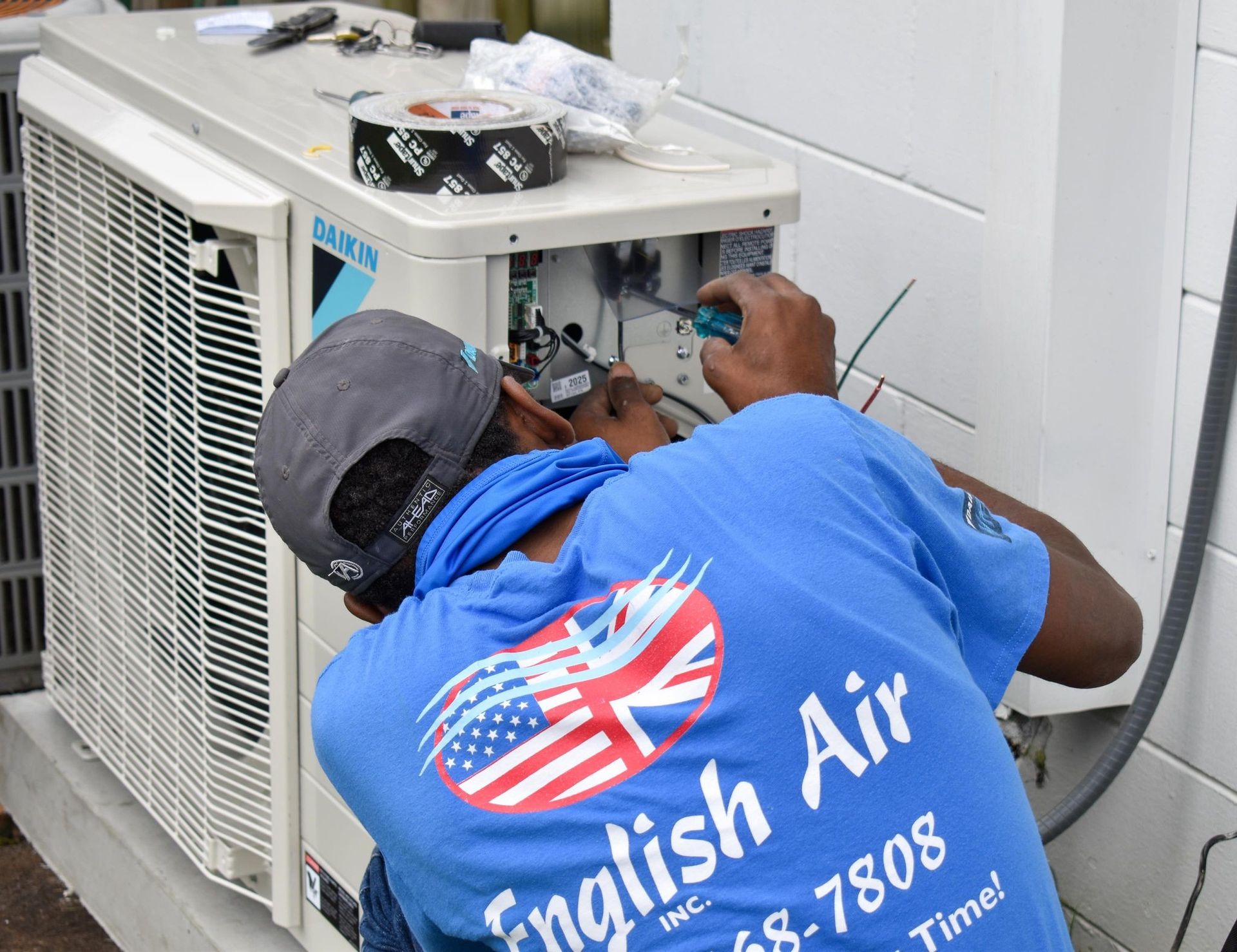 Person in mask and blue shirt posing beside an open HVAC unit with exposed machinery and controls.