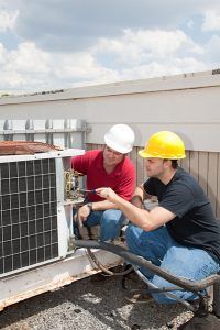 Two workers in hard hats inspecting an outdoor HVAC unit on a rooftop