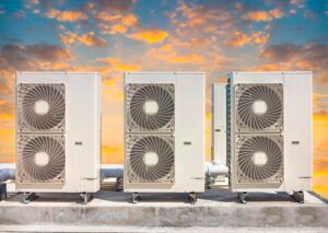 Three outdoor HVAC units on a rooftop at sunset with orange clouds overhead
