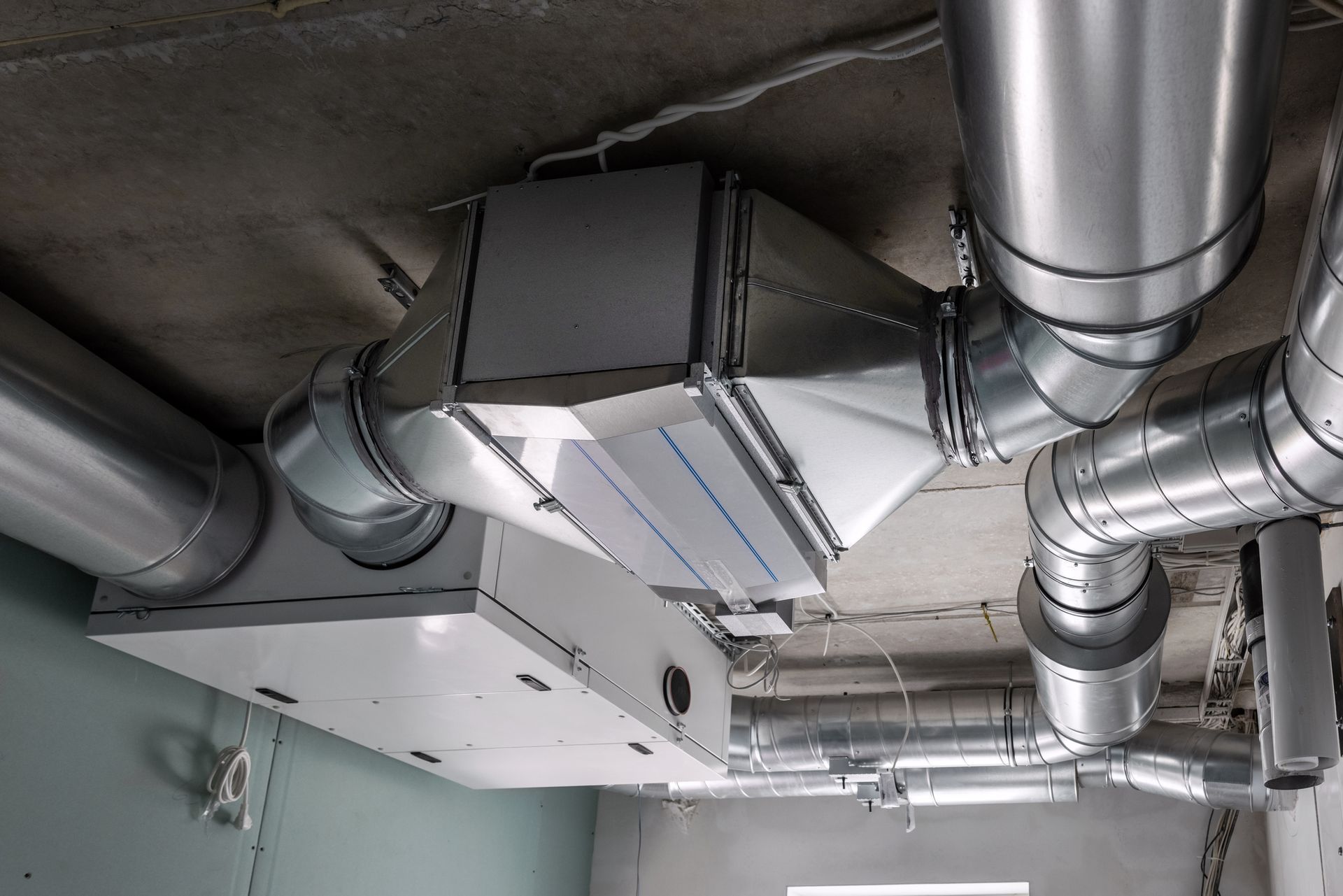 Ceiling-mounted HVAC ducts and vents in an industrial interior, with silver metal pipes and white insulation.
