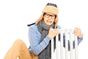 Person in winter clothes and glasses leaning on a white radiator, smiling on a white background