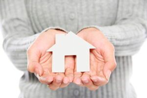 Hands holding a white house icon on a gray sweater background