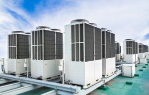 Row of large rooftop HVAC units on a metal platform under a blue sky
