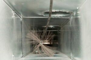 A metal ventilation duct with dust, tangled wires, and a cable hanging through the center.