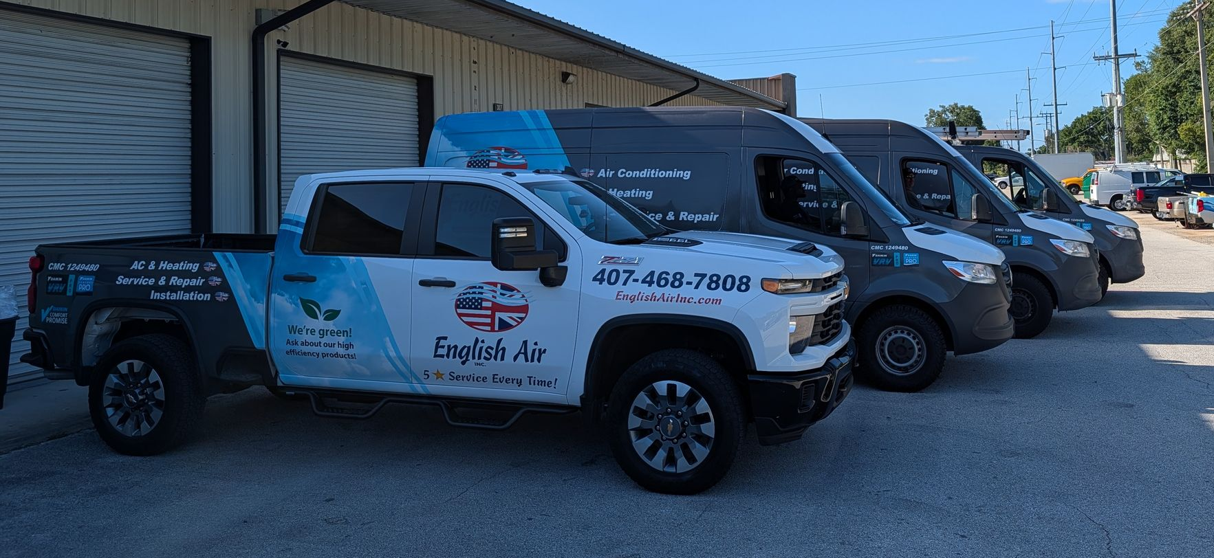 White pickup trucks with company logos parked outside a metal-sided building on a sunny day