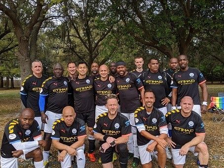 Soccer team posing outdoors in matching black jerseys, with trees in the background