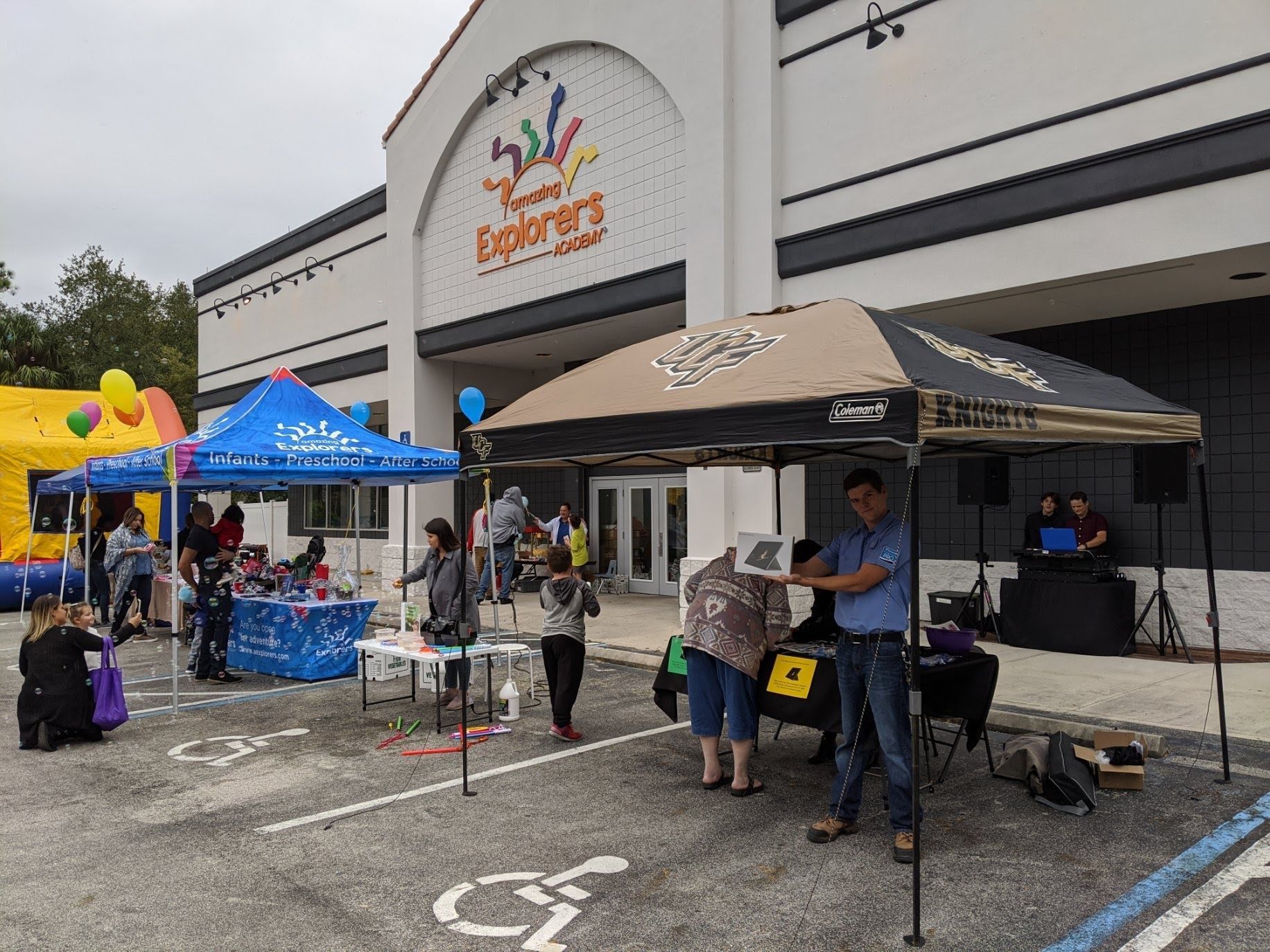 Outdoor community event with blue and tan tents, tables, and people outside a store entrance