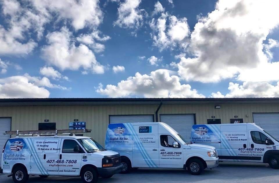 Three white service vans with blue graphics parked outside a warehouse under a cloudy sky