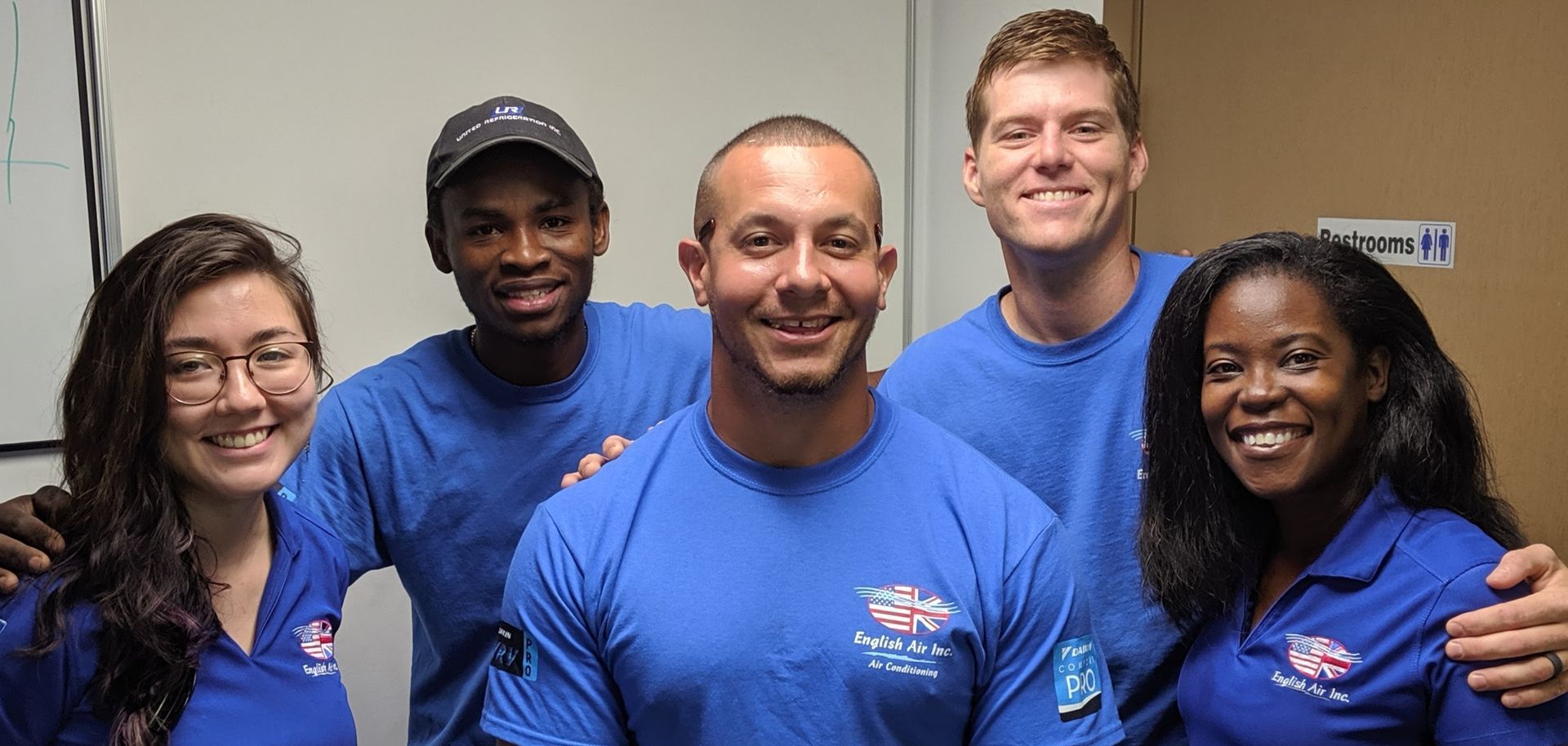 Five smiling people in blue shirts standing together indoors