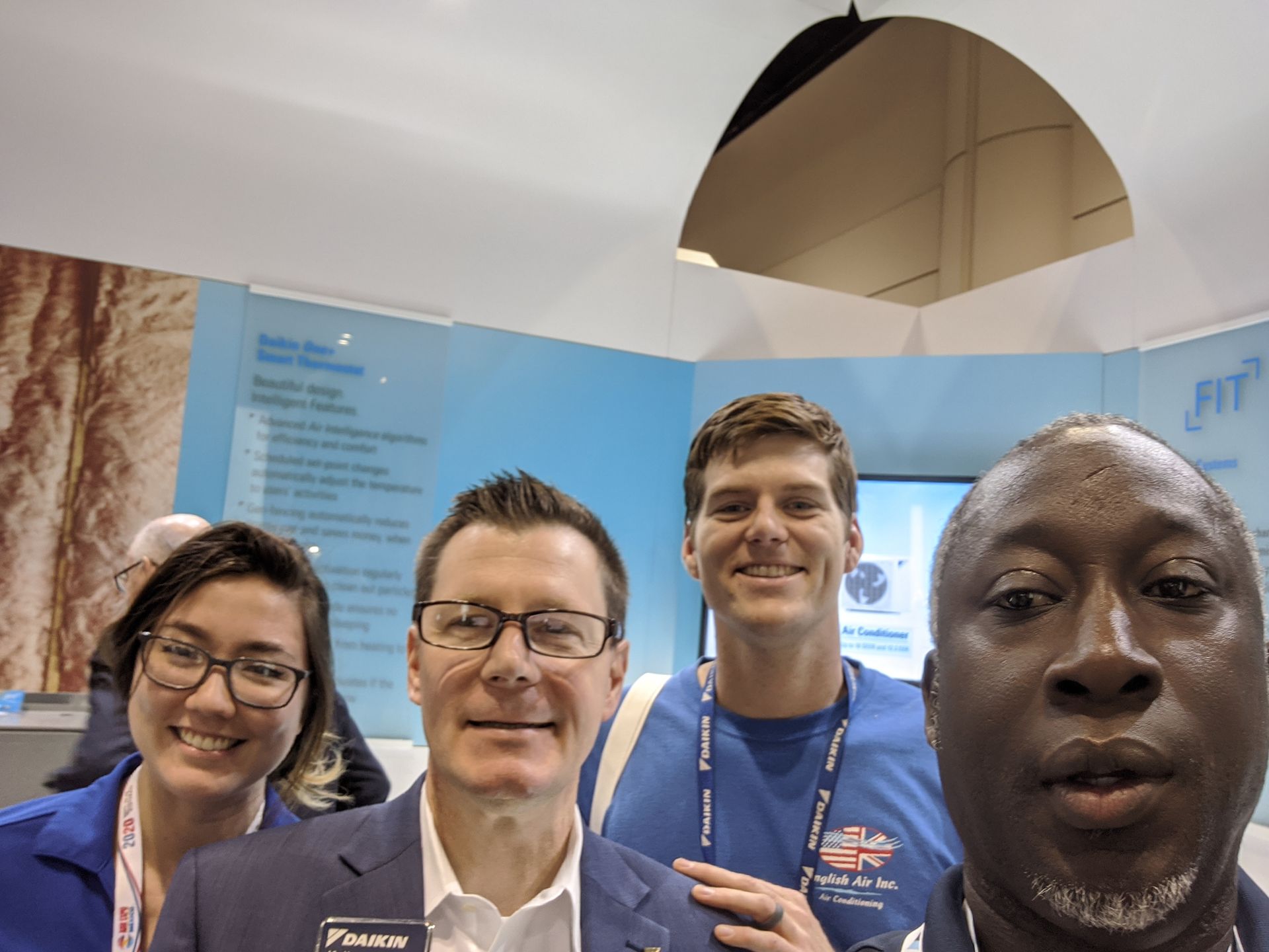 Four people smiling at a conference booth with a blue backdrop