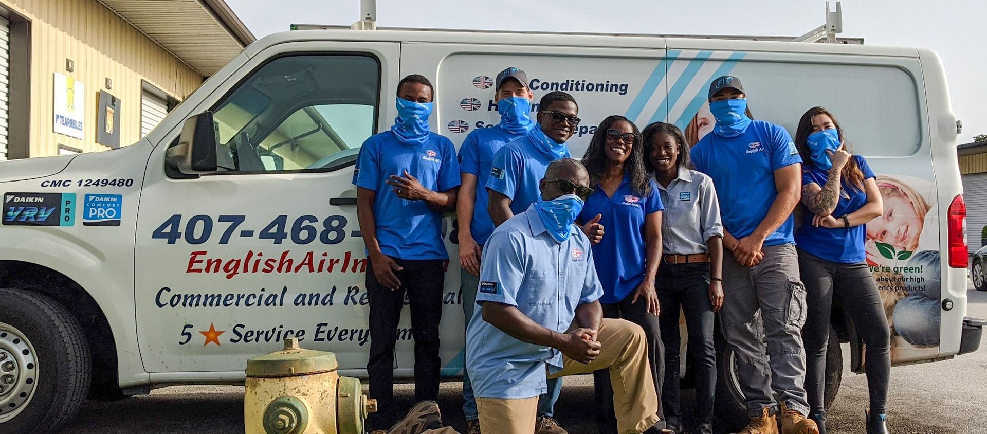 Group in blue shirts posing beside a white work van with company branding and phone number.