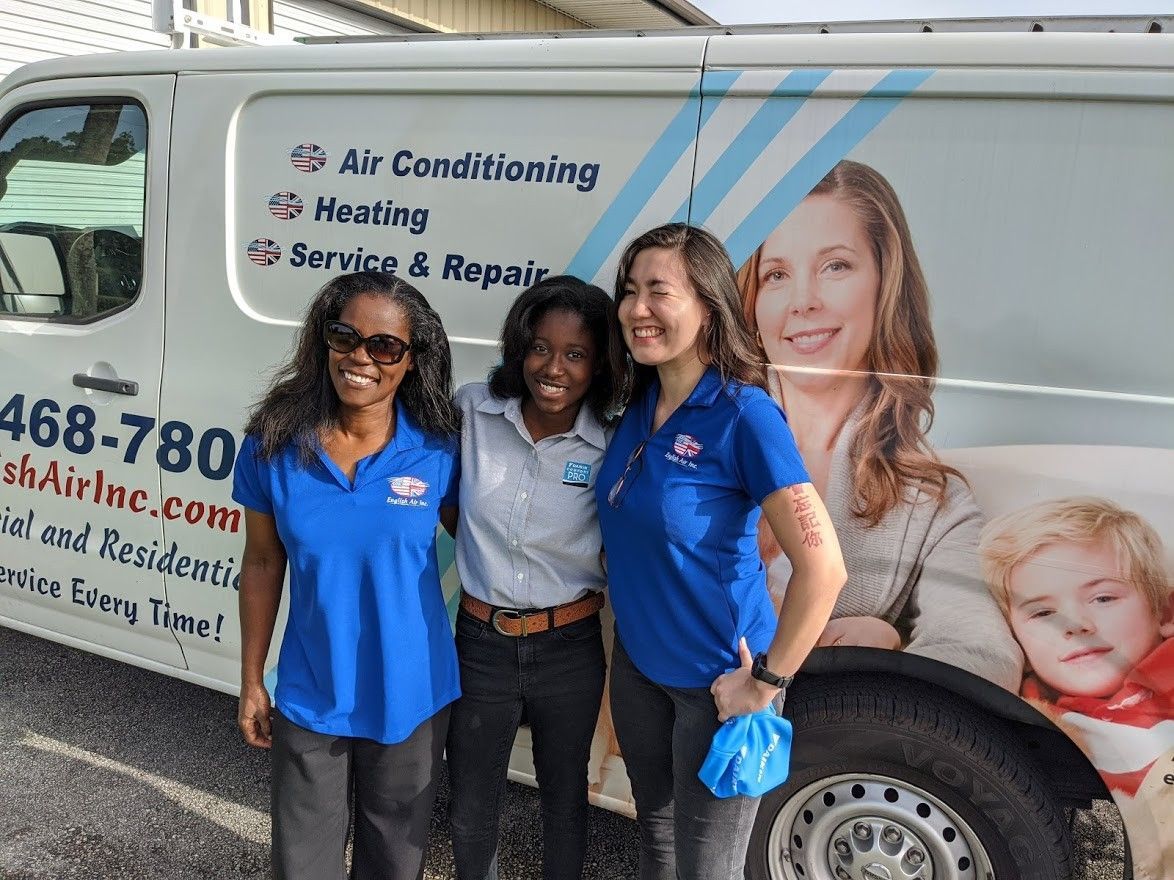 Three women in blue shirts standing beside an air conditioning service van with company branding