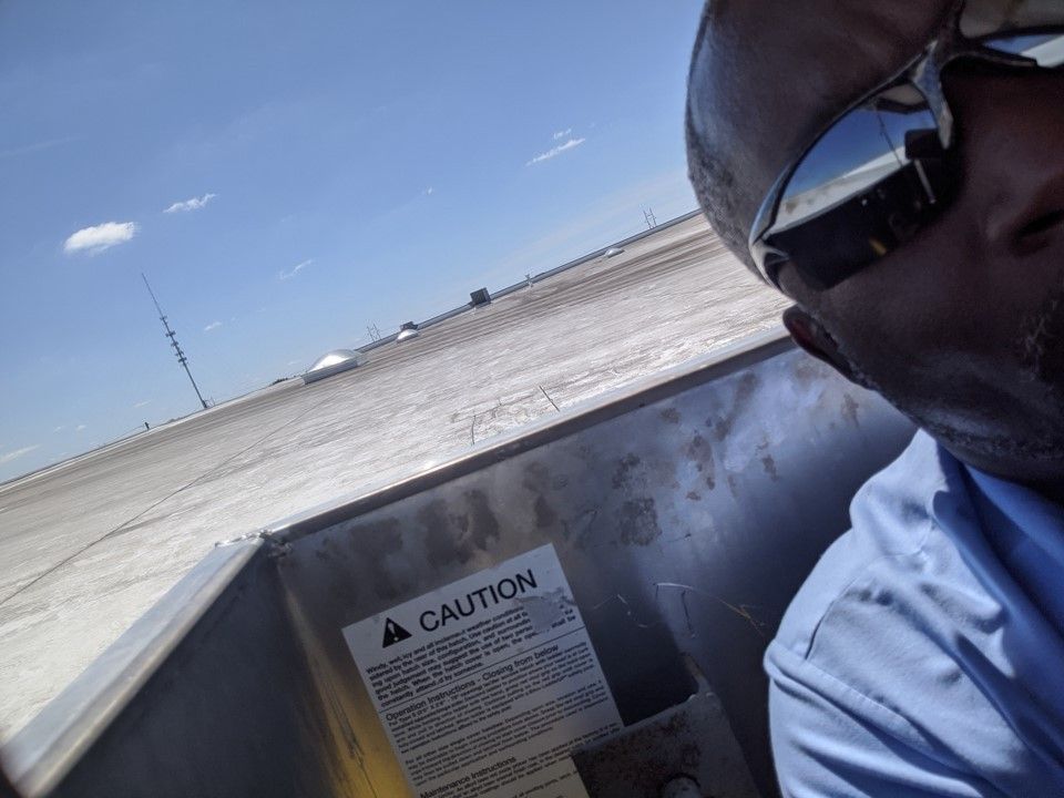Man in sunglasses on a boat beside a caution sign, with open water and shoreline in the background
