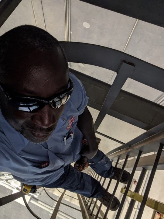 Man standing on a metal staircase, wearing sunglasses and a blue shirt, viewed from above.