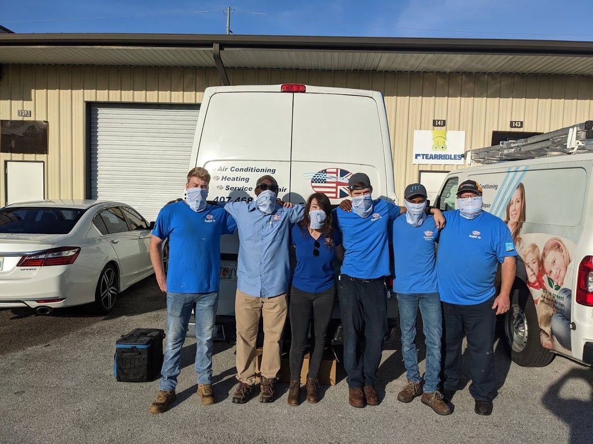 Six people in blue shirts pose in a parking lot beside vans and a white car.