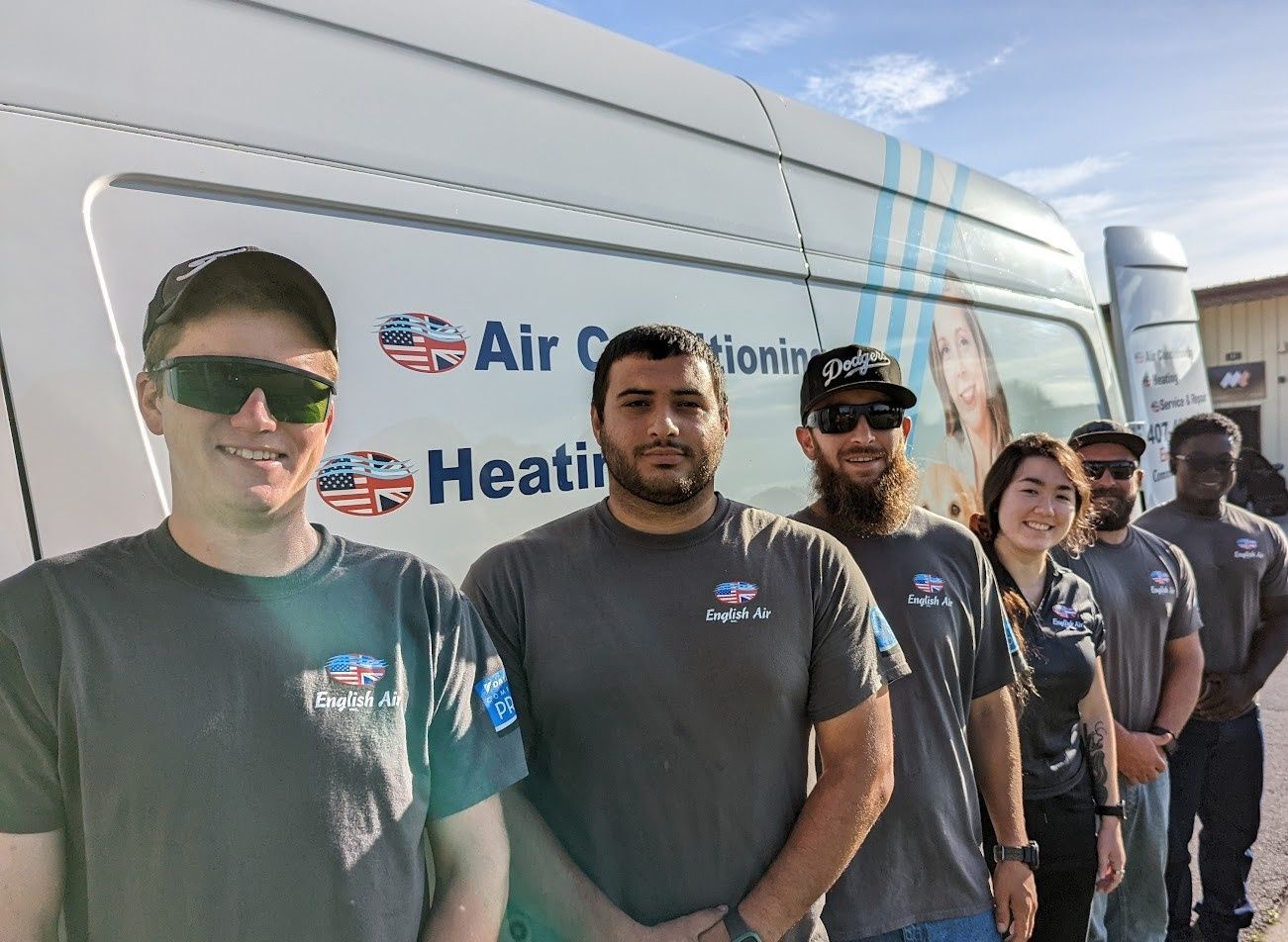 Five workers in dark shirts stand beside an Air Conditioning & Heating service van.
