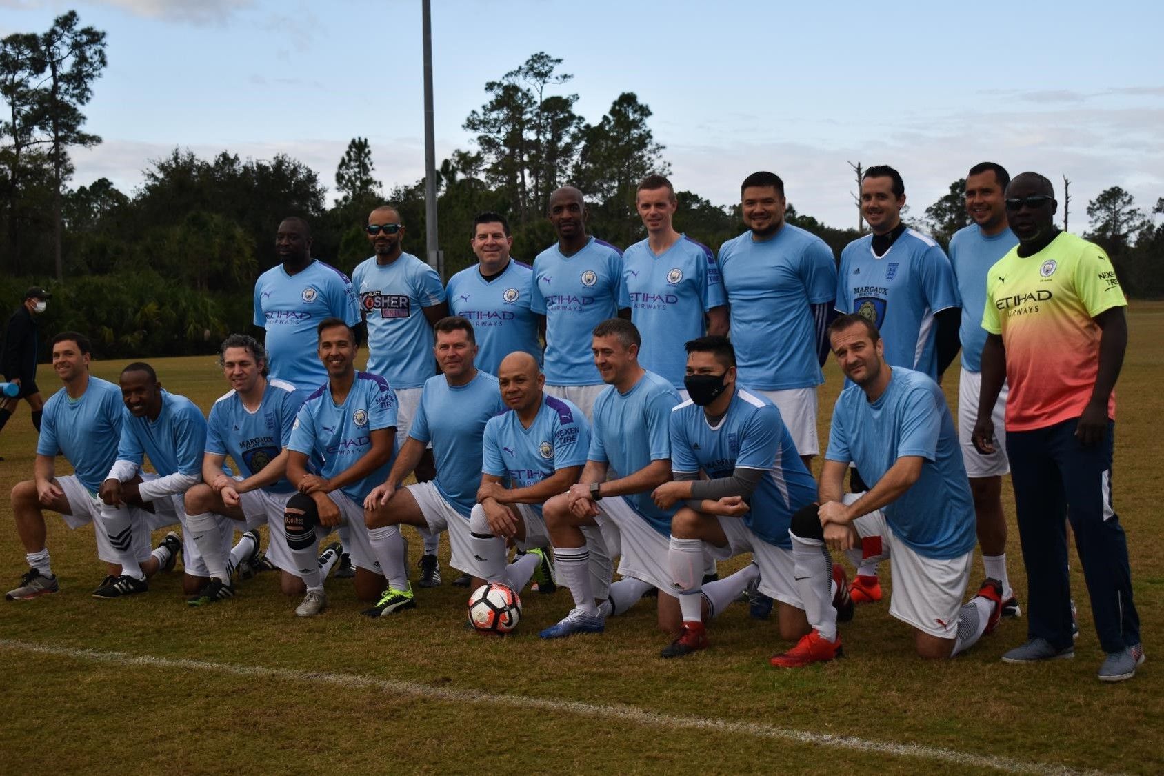 Soccer team in light blue jerseys posing on a grassy field with a referee in yellow