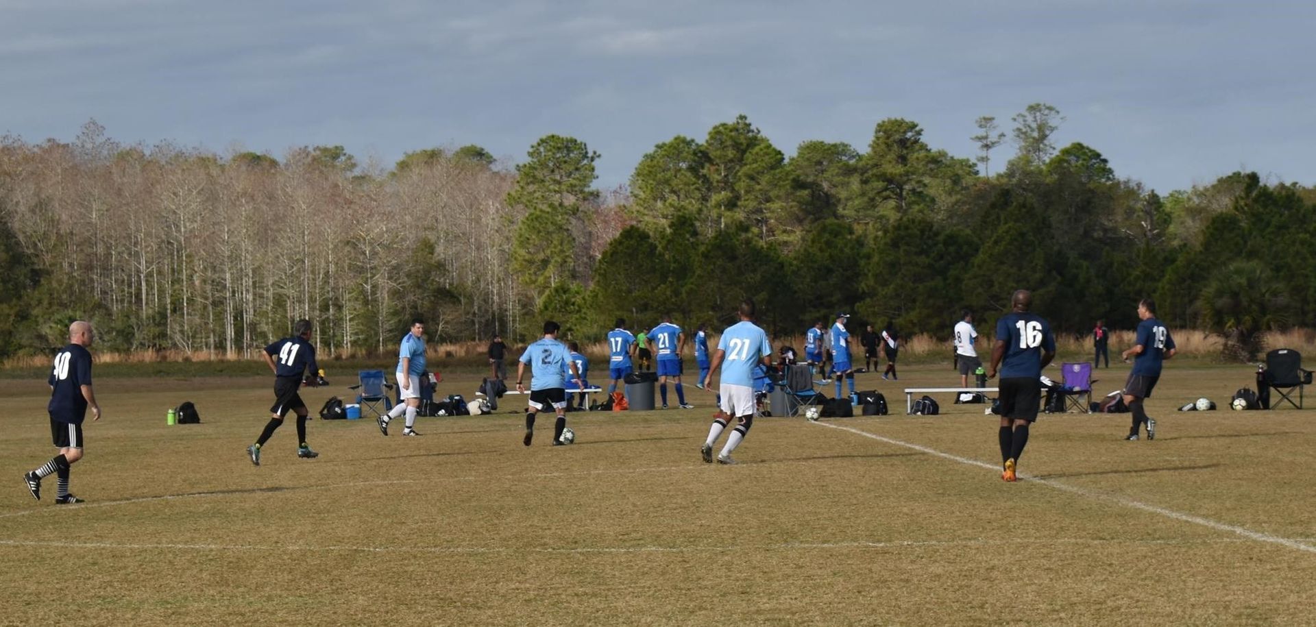 Soccer practice on a grassy field with players in blue jerseys and black uniforms under a clear sky