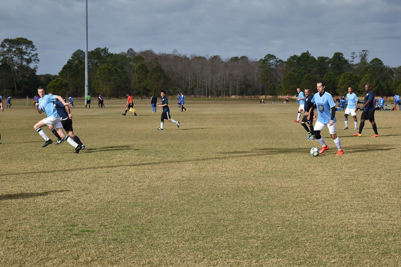 Soccer players in blue and black jerseys competing on a grassy field under a clear sky