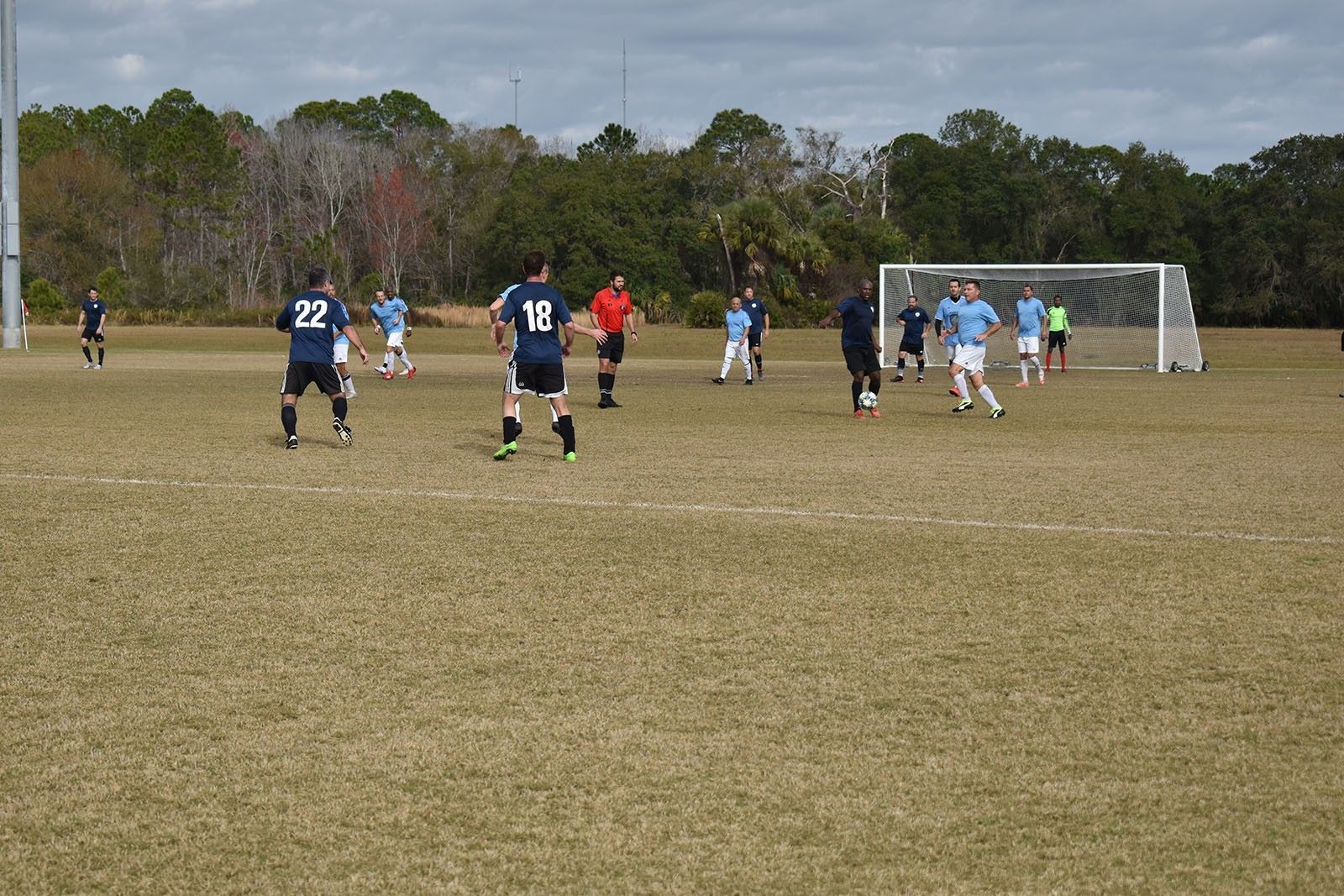 Soccer players on a muddy field near the goal, with spectators in the background