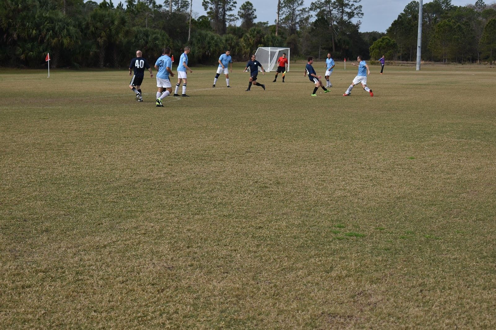 Soccer players in light blue and white uniforms compete on a grassy field near a goal.