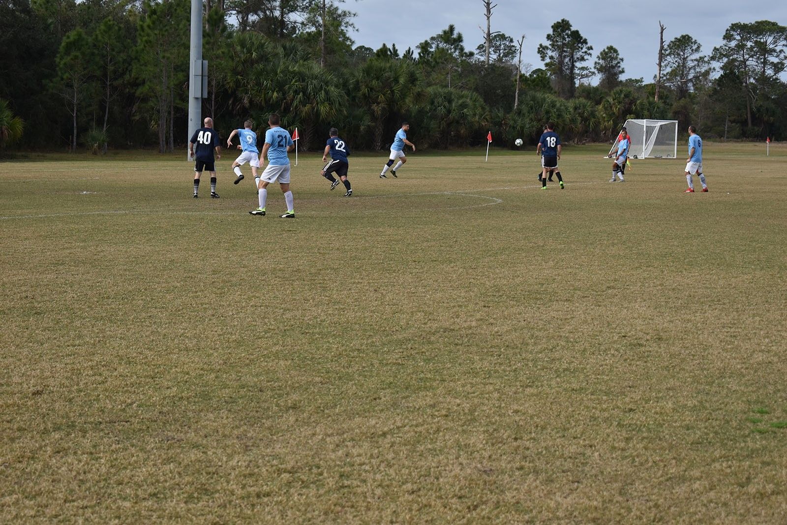 Youth soccer game on a grassy field, with players in light blue and dark uniforms near the goal.