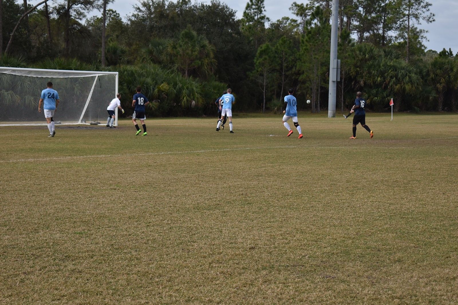 Soccer game near the goal on a grassy field, with players in blue and black uniforms.