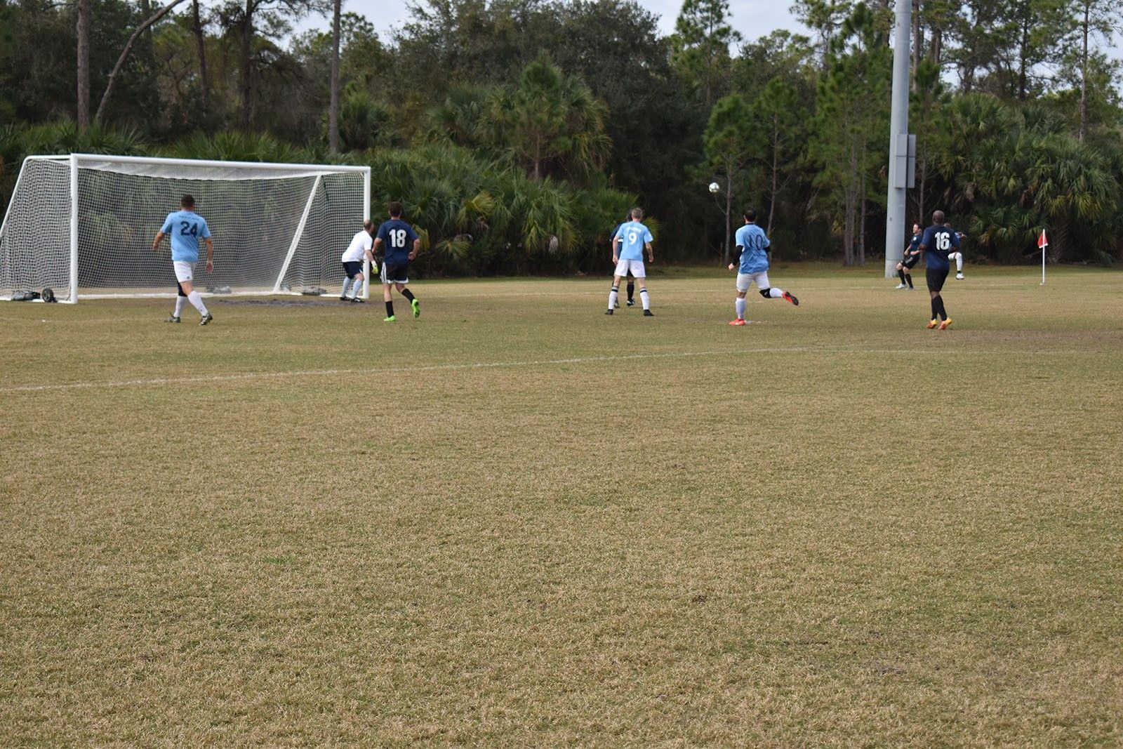 Soccer match near the goal on a grassy field, with players in blue and black chasing the ball.