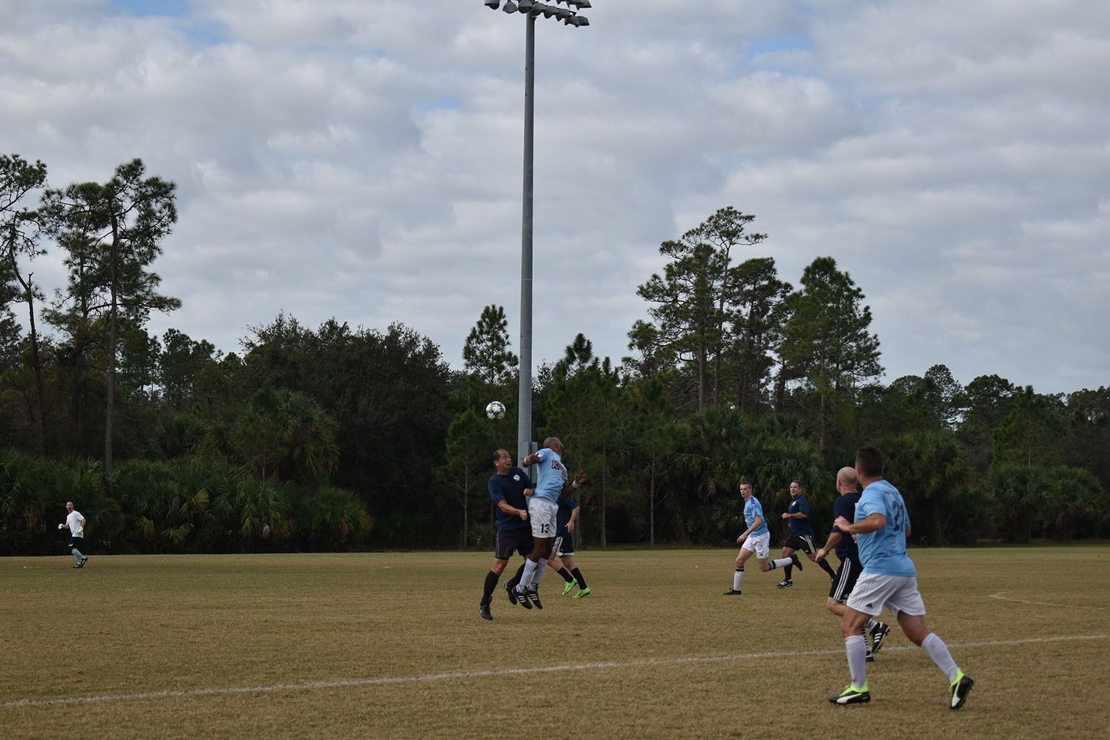 Soccer players in blue uniforms compete on a grassy field under overcast skies.